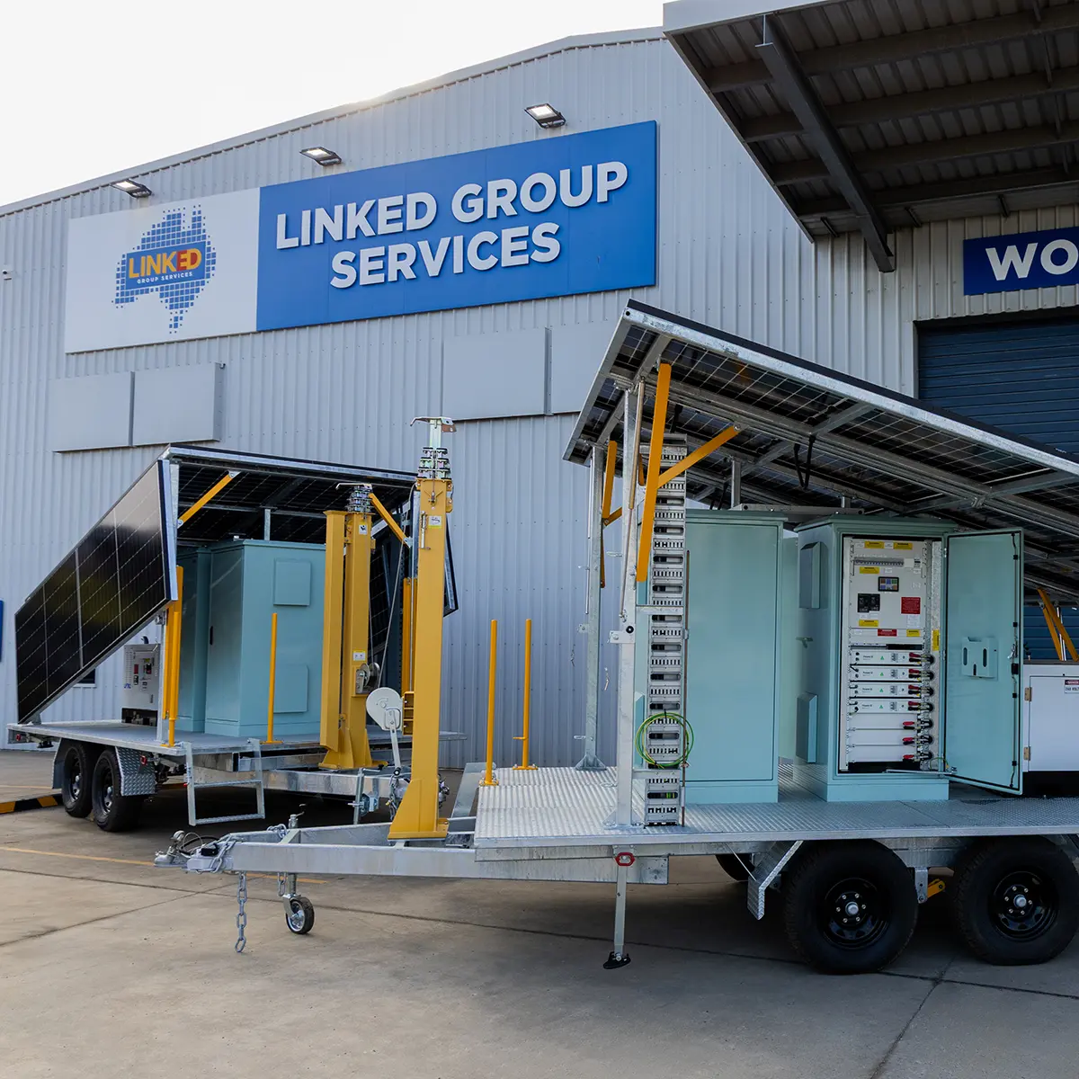 Two EC0G3N T4800 trailers with solar panels and communication equipment parked outside a Linked Group Services building, ready for mine site deployment.