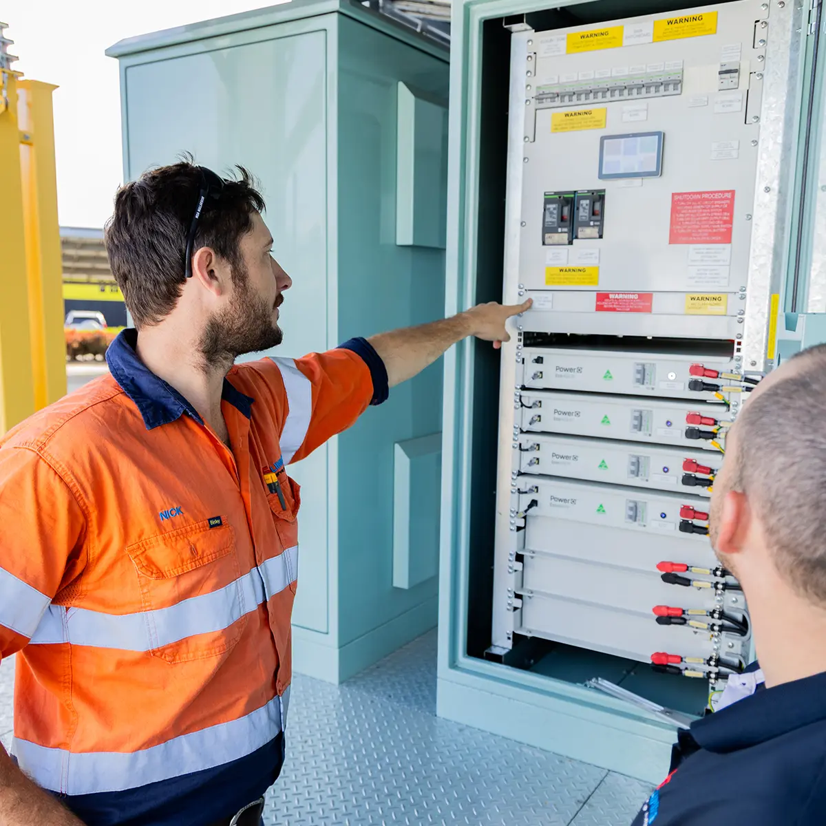 Two CSE Linked employees in high-visibility workwear inspecting an open electrical cabinet with control panel components, part of a solar energy system in a mining setting.